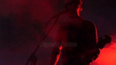 Hipster adam grupta bas gitar çalan ve duman sahnede şarkı söylüyor. Ağır çekim. Müzik, ses, müzik grubu, kavram.