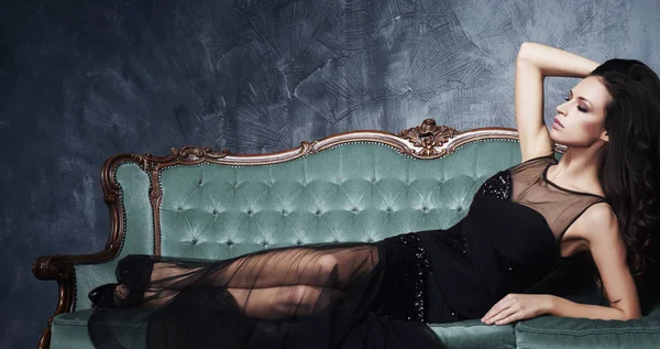 美丽的女人坐在沙发上的黑色礼服 — 图库照片