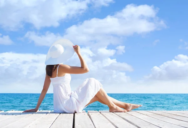 Όμορφο, ελκυστικό μοντέλο ποζάρει σε λευκό φόρεμα σε μια ξύλινη αποβάθρα. Θάλασσα και ουρανό φόντο. Διακοπές, τα ταξίδια και το θέρετρο έννοια. — Φωτογραφία Αρχείου
