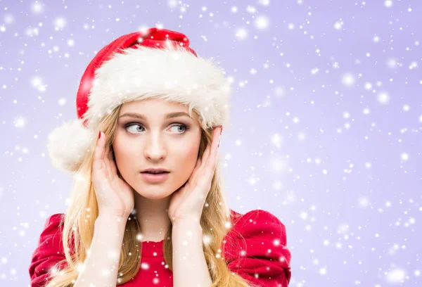 年轻美丽的女人的肖像戴着圣诞老人的帽子对蓝色背景与雪花 圣诞节和冬季假期概念 — 图库照片