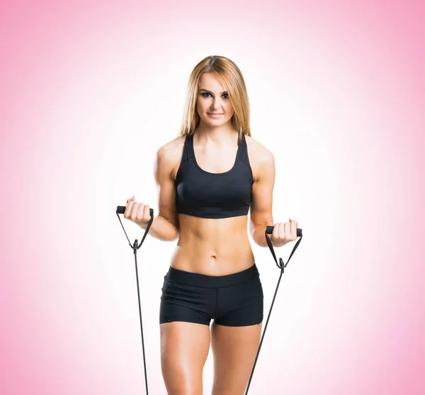 Fit, gezond en sportief meisje in sportkleding expander oefening doet roze achtergrond. — Stockfoto