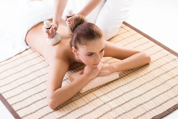 Mujer joven, hermosa y saludable relajarse en el salón de spa. Terapia de aroma oriental tradicional y tratamientos de masaje con bolas de hierbas . — Foto de Stock