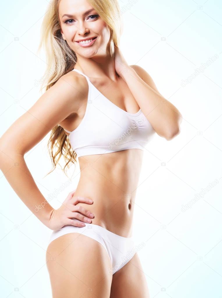 fit and sporty blonde woman in white lingerie over light background. Sport, fitness, diet, weight loss and healthcare concept