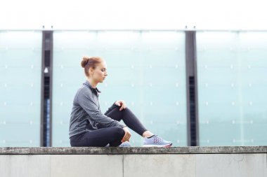 Genç, uygun ve sportif kadın beton sınırda oturuyordu. Fitness, spor, kentsel koşu ve sağlıklı yaşam konsepti.