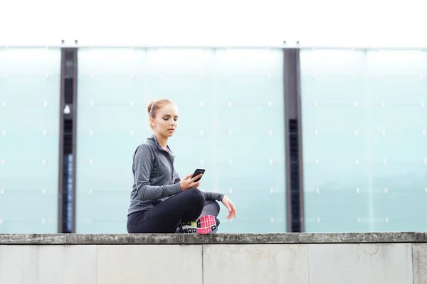 Genç Uygun Sportif Kadın Telefon Ile Beton Sınır Üzerinde Oturuyordu — Stok fotoğraf