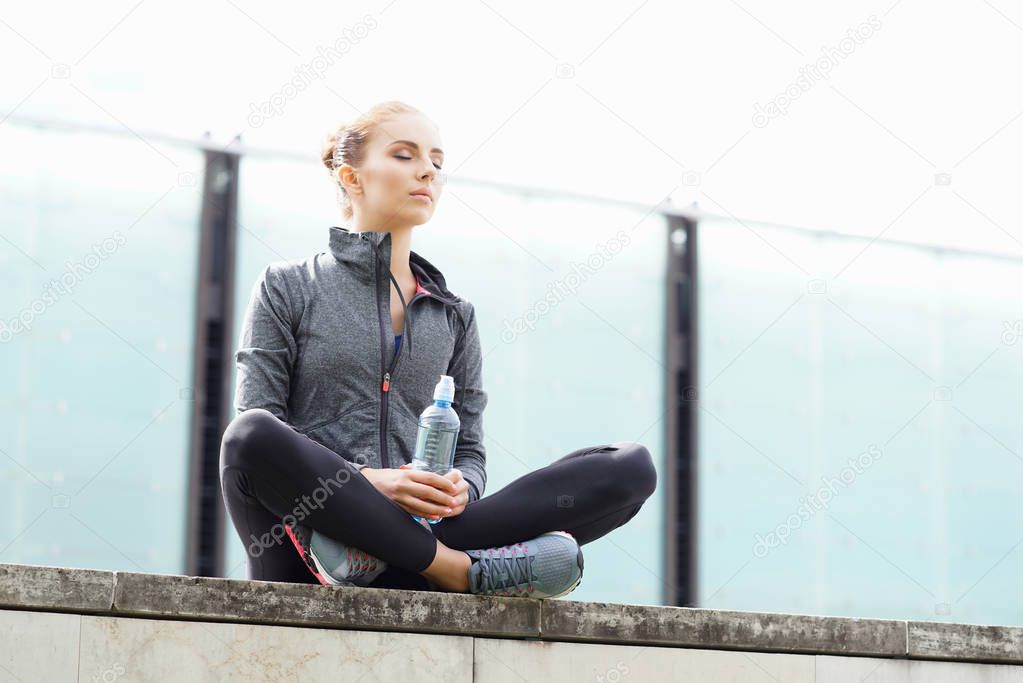 Young, fit and sporty woman sitting on a concrete border. Fitness, sport, urban jogging and healthy lifestyle concept.