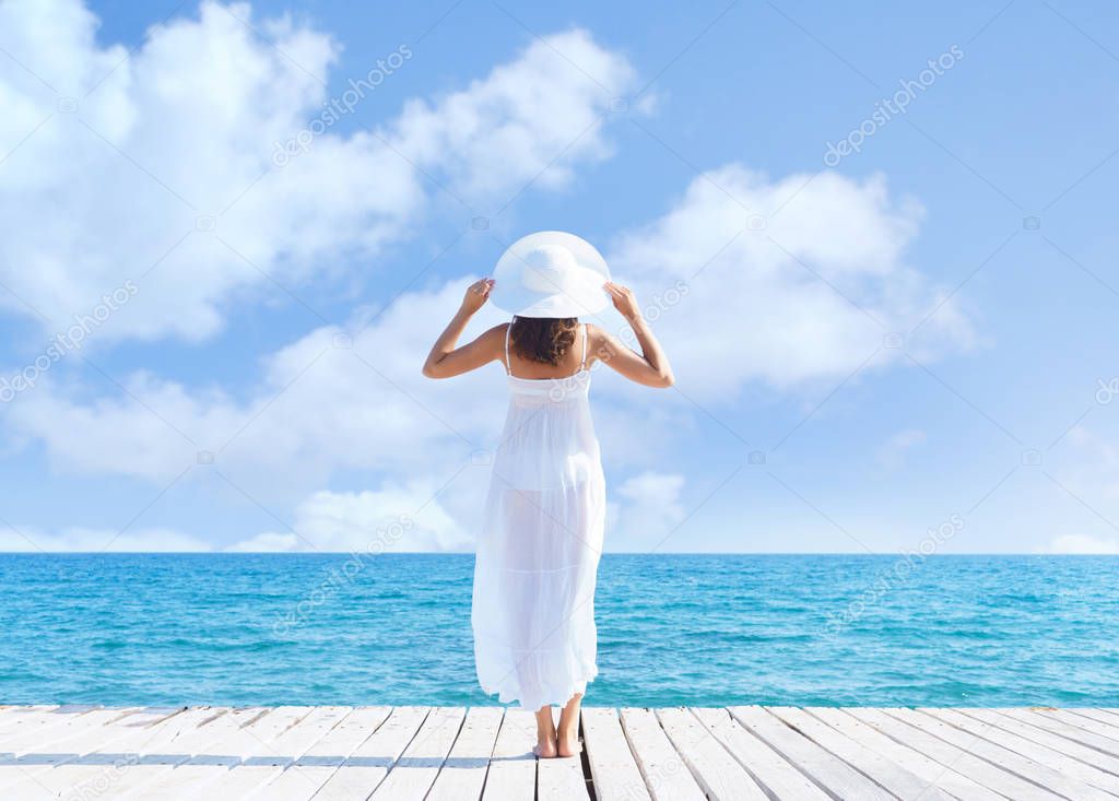 Back view of a young woman standing on a pier.  Sea and sky background. Vacation and traveling concept.