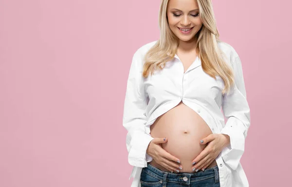 スタジオで妊娠中の若い女性はピンクの背景に彼女の美しいおなかの胃を受け入れます 出産の概念 — ストック写真