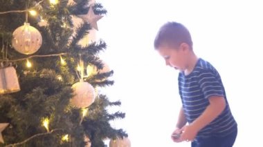  Küçük çocuk Noel ağacını toplar ve ışıklarla süslüyor. Çocuk evde yeni yıla hazırlanıyor. Mevsimlik kavram