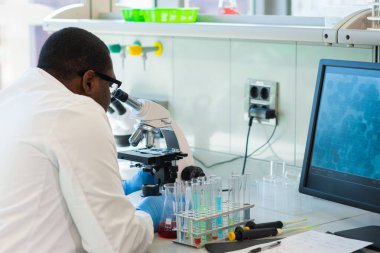 Araştırma laboratuvarında çalışan Afro-Amerikan tıp doktoru. Bilim asistanı ilaç deneyleri yapıyor. Laboratuvar araçları: mikroskop, test tüpleri, ekipman. Kimya, tıp, biyokimya
