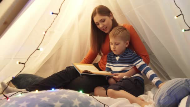 晚上小男孩在家里孩子们的帐篷里玩耍 妈妈在看童话书 在游戏室里快乐的高加索小孩 — 图库视频影像