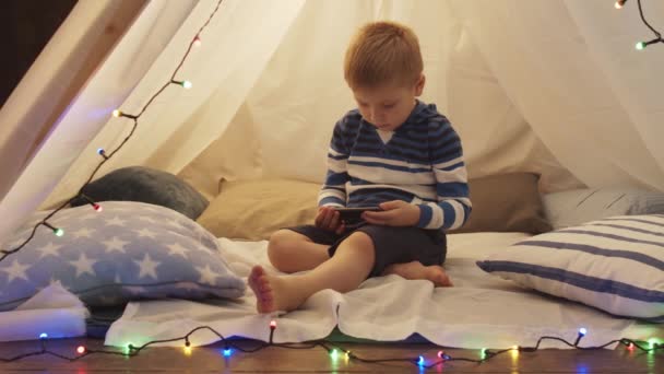 夕方には子供のテントの中でスマホで遊んでいる男の子 幸せなCaucasian子供でザPlayroom — ストック動画