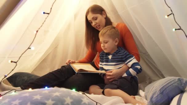 晚上小男孩在家里孩子们的帐篷里玩耍 妈妈在看童话书 在游戏室里快乐的高加索小孩 — 图库视频影像