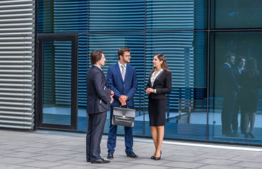 Modern ofis binasının önünde konuşan emin işadamlarının. İşadamlarının ve iş kadınının işi var. Bankacılık, profesyonel iş ve finansal piyasa konsepti.