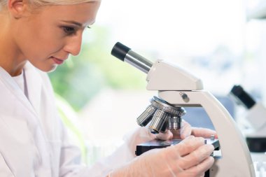 Tıp doktoru araştırma laboratuarında çalışıyor. Bilim asistanı ilaç deneyi yapıyor. Laboratuar araçları: mikroskop, test tüpleri, ekipman. Kimya, tıp, biyokimya, biyoteknoloji ve