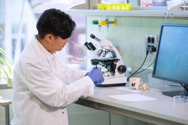 Laboratuarda çalışan bir bilim adamı. Asya doktoru tıbbi araştırma yapıyor. Laboratuar araçları: mikroskop, test tüpleri, ekipman. Biyoteknoloji, kimya, bilim, deney ve sağlık konsepti. Gün ışığı