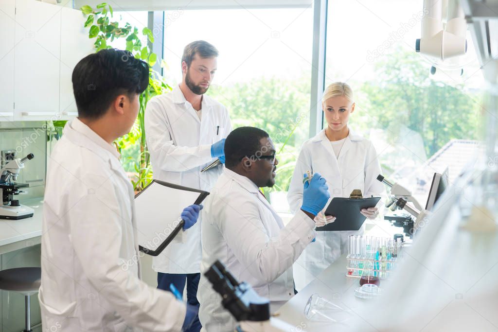 Scientist and students working in lab. Doctor teaching interns to make blood analyzing research. Laboratory tools: microscope, test tubes, equipment. Biotechnology, chemistry, bacteriology, virology