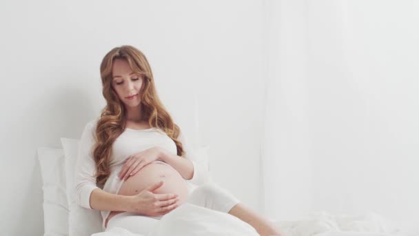 Счастливая Беременная Женщина Трогает Свой Красивый Живот Сидя Постели Беременность — стоковое видео