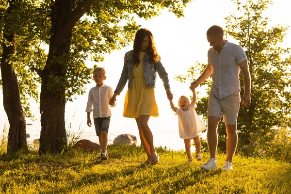 Mutlu bir aile denize yakın yürüyor. Kırsal kesimdeki tarla ve ağaçlar. Gün batımı veya gün doğumu sıcak renkler. Sevgi dolu ebeveynler ve güzel çocuklar. Aşk ve ebeveynlik kavramı.
