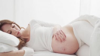 Mutlu hamile kadın yatakta uzanmış güzel karnına dokunuyor. Hamilelik, annelik ve beklenti konsepti.