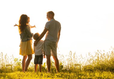 Mutlu sevgi dolu aile gün batımında dışarıda yürüyor. Baba, anne, oğul ve kız. Deniz ve alan arkaplanı