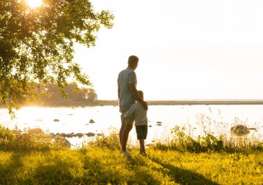 Babası ve küçük oğlu. Mutlu sevgi dolu aile gün batımında dışarıda yürüyor. Deniz ve alan arkaplanı