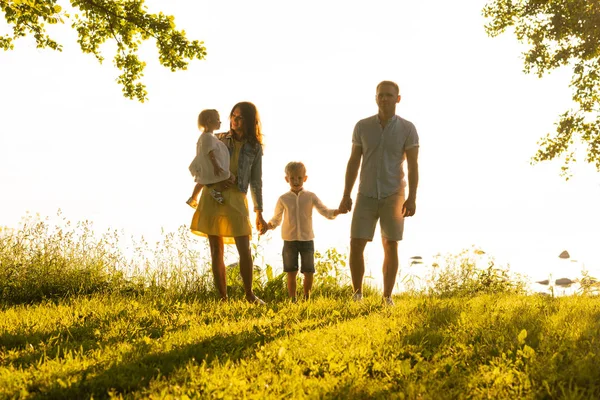 Mutlu sevgi dolu aile gün batımında dışarıda yürüyor. Baba, anne, oğul ve kız. Deniz ve alan arkaplanı
