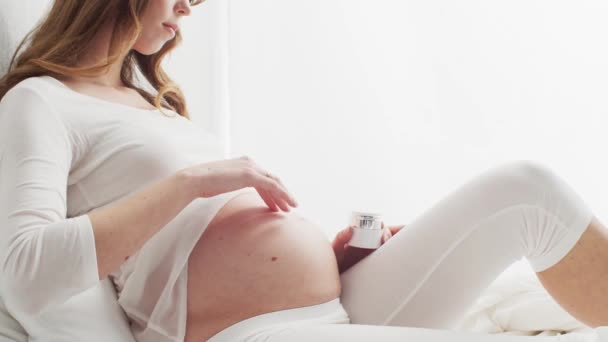 Lycklig Gravid Kvinna Applicera Grädde Hennes Vackra Mage Sitter Sängen — Stockvideo
