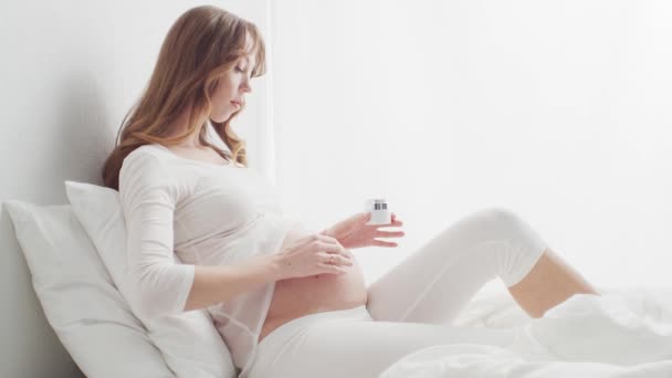 Feliz Mulher Grávida Aplicando Creme Sua Bela Barriga Sentada Cama — Vídeo de Stock