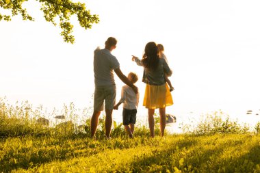 Mutlu sevgi dolu aile gün batımında dışarıda yürüyor. Baba, anne, oğul ve kız. Deniz ve alan arkaplanı