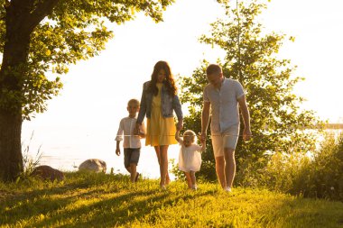 Mutlu sevgi dolu aile gün batımında dışarıda yürüyor. Baba, anne, oğul ve kız. Deniz ve alan arkaplanı