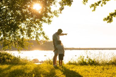 Babası ve küçük oğlu. Mutlu sevgi dolu aile gün batımında dışarıda yürüyor. Deniz ve alan arkaplanı