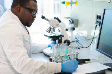 Araştırma laboratuvarında çalışan Afro-Amerikan tıp doktoru. Bilim asistanı ilaç deneyleri yapıyor. Laboratuvar araçları: mikroskop, test tüpleri, ekipman. Kimya, tıp, biyokimya