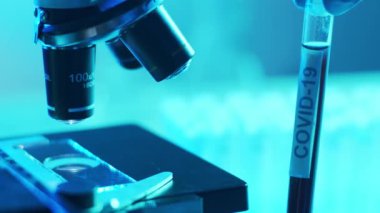 Mikroskop ve üzerinde kan ve virüs olan laboratuvar tüpü. Bilimsel laboratuvar yakın plan. Salgın hastalıklar, sağlık hizmetleri, aşı araştırmaları ve Coronavirus covid-19 test konsepti.