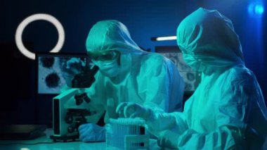 Laboratuvarda çalışan koruyucu giysi ve maskeli bilim adamları laboratuvar ekipmanları kullanıyorlardı: mikroskop, test tüpleri. Coronavirus covid-19 tehlike, ilaç keşfi, bakteri bilimi ve virüs bilimi
