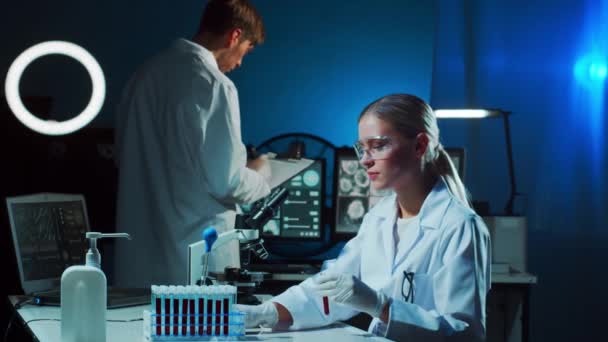 研究室で働いている医学者 血液分析の研究をするために医師の先生のインターン 研究室のツール 顕微鏡 試験管 コロナウイルス バイオテクノロジー 細菌学 ウイルス学 — ストック動画