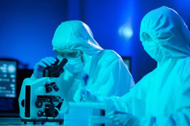 Laboratuvarda çalışan koruyucu giysi ve maskeli bilim adamları laboratuvar ekipmanları kullanıyorlardı: mikroskop, test tüpleri. Coronavirus covid-19 tehlike, ilaç keşfi, bakteri bilimi ve virüs bilimi