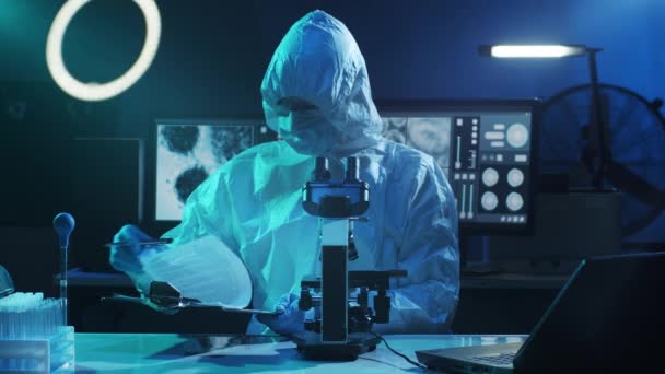 研究室の機器を使用して研究室で働く保護スーツやマスクの科学者 顕微鏡 試験管 コロナウイルスSars Cov 2の危険性 医薬品の発見 細菌学とウイルス学 — ストック動画