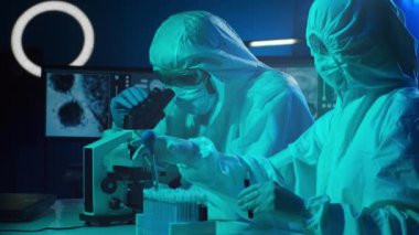 Laboratuvarda çalışan koruyucu giysi ve maskeli bilim adamları laboratuvar ekipmanları kullanıyorlardı: mikroskop, test tüpleri. Coronavirus covid-19 tehlike, ilaç keşfi, bakteri bilimi ve virüs bilimi
