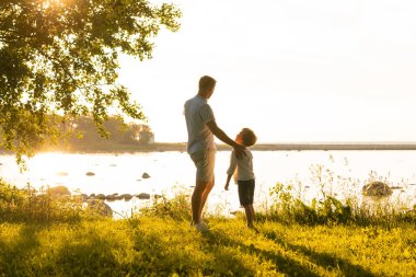 Babası ve küçük oğlu. Mutlu sevgi dolu aile gün batımında dışarıda yürüyor. Deniz ve alan arkaplanı