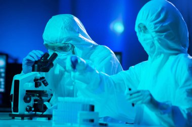 Laboratuvarda çalışan koruyucu giysi ve maskeli bilim adamları laboratuvar ekipmanları kullanıyorlardı: mikroskop, test tüpleri. Coronavirus covid-19 tehlike, ilaç keşfi, bakteri bilimi ve virüs bilimi