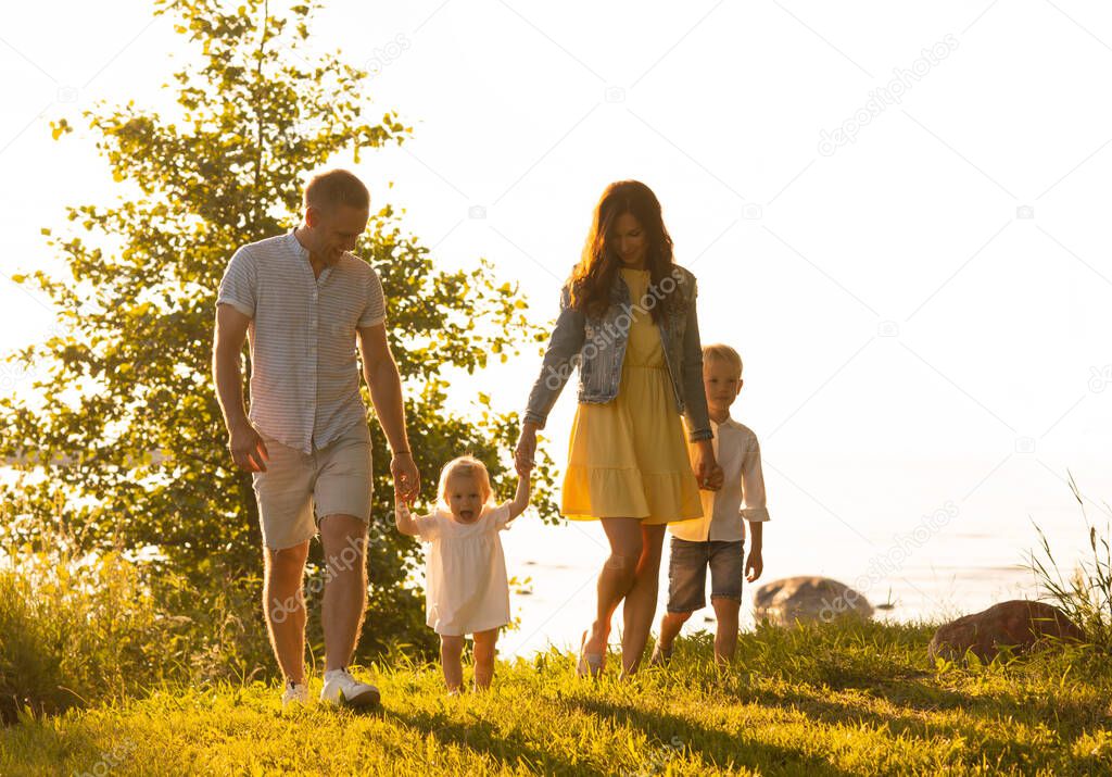 Happy loving family walking outdoor in the light of sunset. Father, mother, son and daughter. Sea and field background