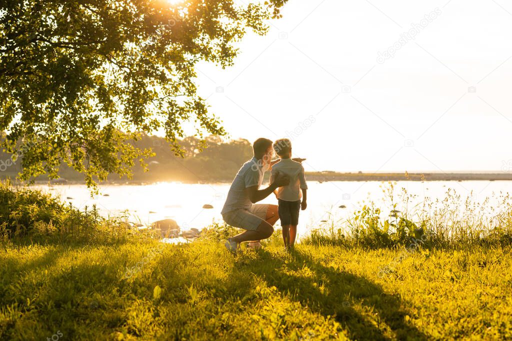 Father and his little son. Happy loving family walking outdoor in the light of sunset. Sea and field background