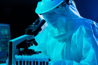 Laboratuvar ekipmanları, mikroskoplar ve test tüpleri kullanarak araştırma laboratuarında çalışan koruyucu giysi ve maskeler giyen bilim adamları. Coronavirus 2019-ncov tehlikesi, ilaç keşfi, bakteriyoloji ve virüs bilimi konsepti.