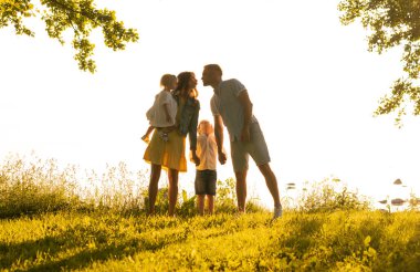 Mutlu sevgi dolu aile gün batımında dışarıda yürüyor. Baba, anne, oğul ve kız. Deniz ve alan arkaplanı