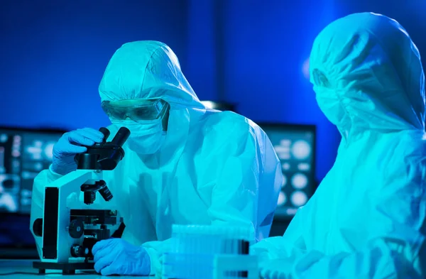 Scientists in protection suits and masks working in research lab using laboratory equipment: microscopes, test tubes. Medicine, coronavirus 2019-ncov infection and vaccine discovery concept.