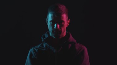 Kapüşonlu bilgisayar korsanı portresi. Neon ışıkta karanlık bir yüz. Veri hırsızlığı, internet dolandırıcılığı, darknet ve siber güvenlik kavramı.