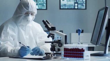 Laboratuvar ekipmanları, mikroskoplar ve test tüpleri kullanarak araştırma laboratuarında çalışan koruyucu giysi ve maskeler giyen bilim adamları. Coronavirus 2019-ncov tehlikesi, ilaç keşfi, bakteri bilimi ve virüs bilimi