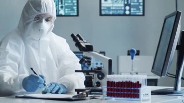 Laboratuvar ekipmanları, mikroskoplar, test tüpleri kullanarak araştırma laboratuarında çalışan koruyucu giysiler ve maskeler giyen bilim adamları. Coronavirus covid-19 tehlike, ilaç keşfi, bakteri bilimi ve virüs bilimi