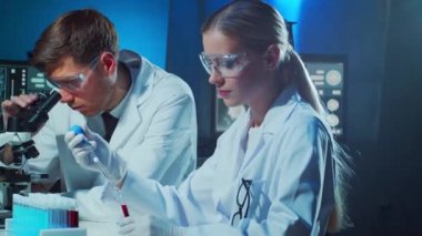 Laboratuvarda çalışan tıp bilimcileri. Doktor stajyerlere kan analizi yapmayı öğretiyor. Laboratuvar aletleri: mikroskop, test tüpleri, ekipmanlar. Koronavirüs, biyoteknoloji, bakteriyoloji, viroloji ve